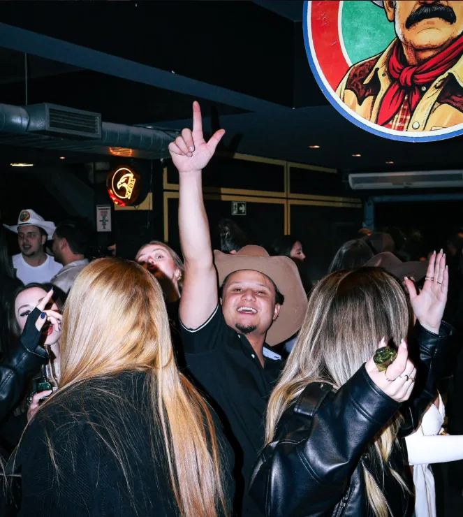 Galera com as mãos para cima e chapéu de cowboy numa noite cheia no Resenha